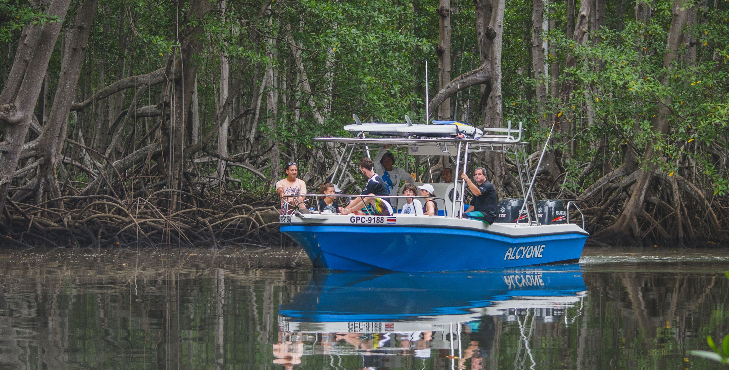A group of kids enjoying a boat tour through a serene mangrove forest in Costa Rica, with intricate root systems visible along the water's edge.
