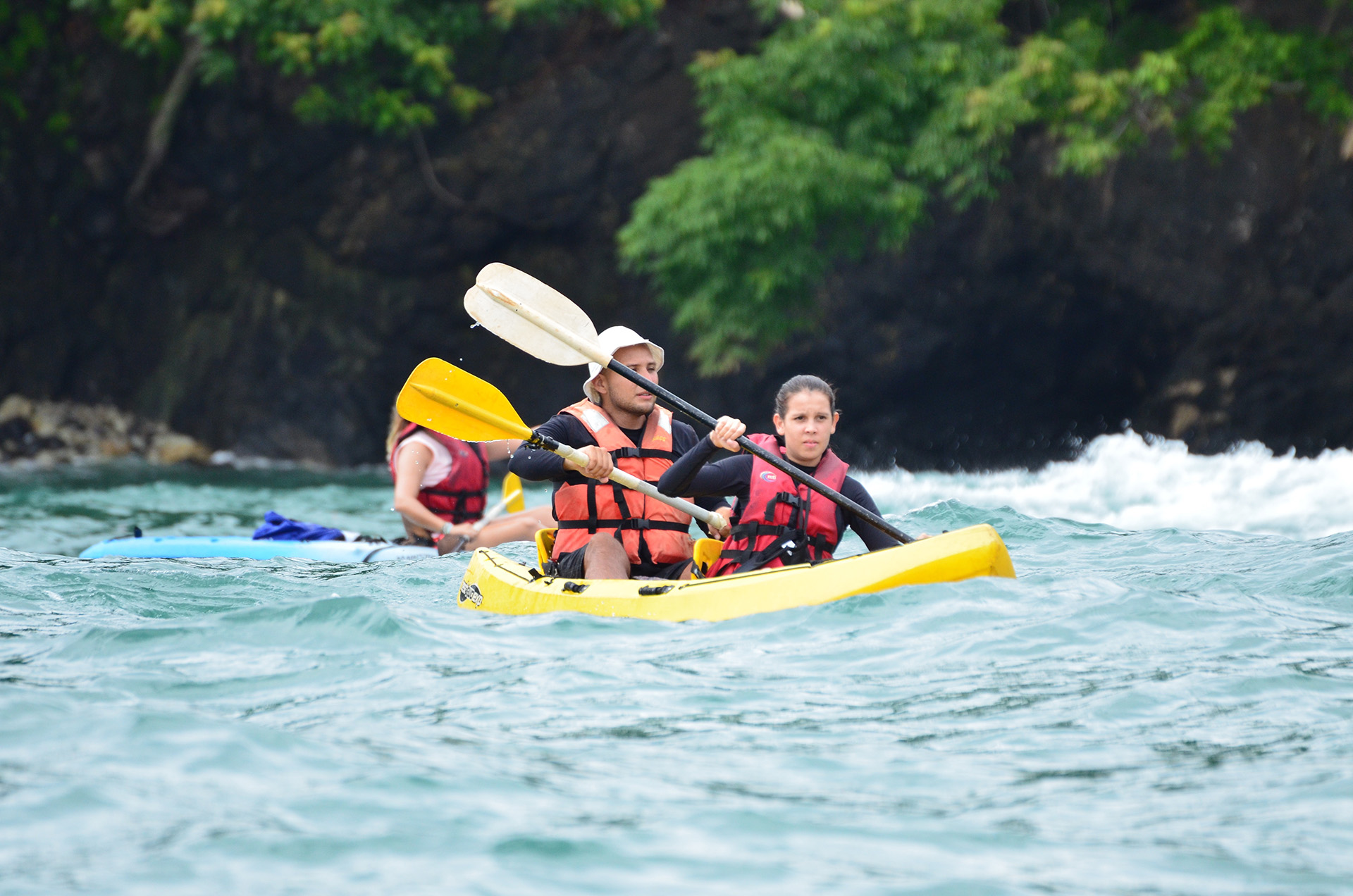 Adventure seekers paddling through the waves in a tandem kayak, exploring the natural beauty along a rocky coastline in Manuel Antonio, Costa Rica.
