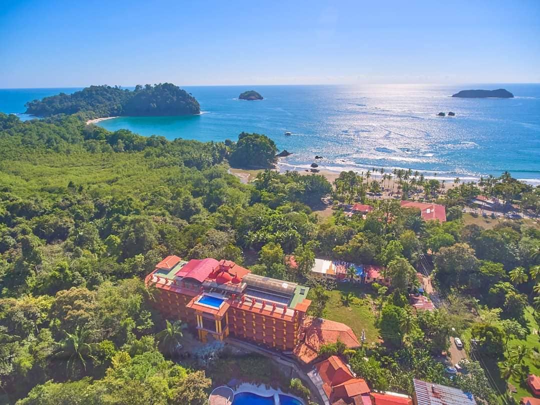 A tranquil coastal retreat: aerial view of a resort nestled between lush greenery and a sparkling blue sea with islands dotting the horizon.