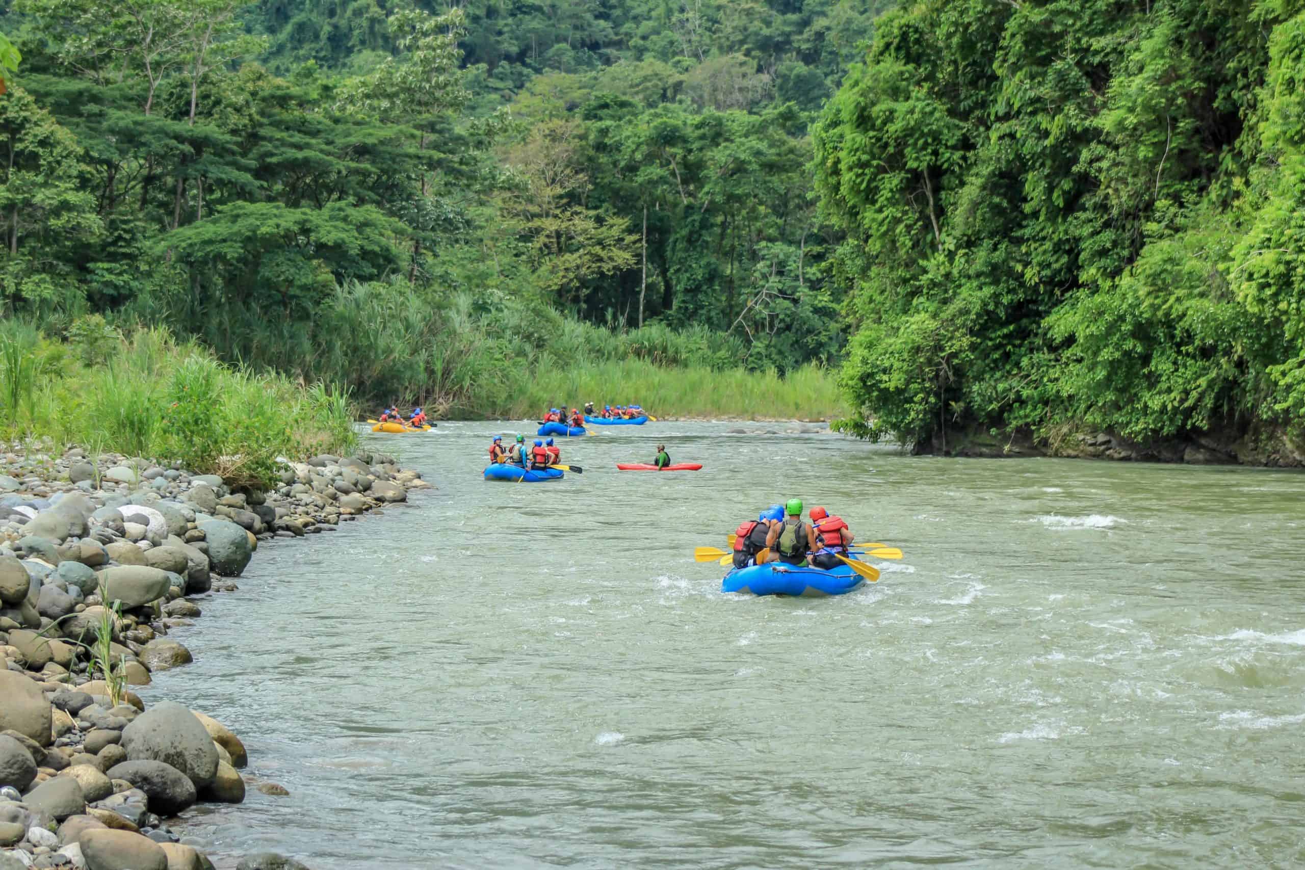 Adventurers in colorful rafts navigating a gently flowing river surrounded by lush greenery in a serene forest setting in Costa Rica.