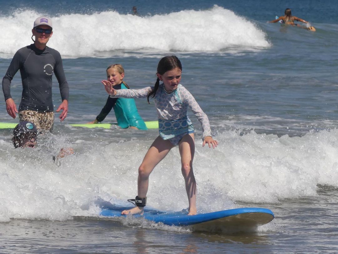 Young girl learns to surf in Manuel Antonio, Costa Rica under the watchful eye of an instructor as the waves gently roll in.