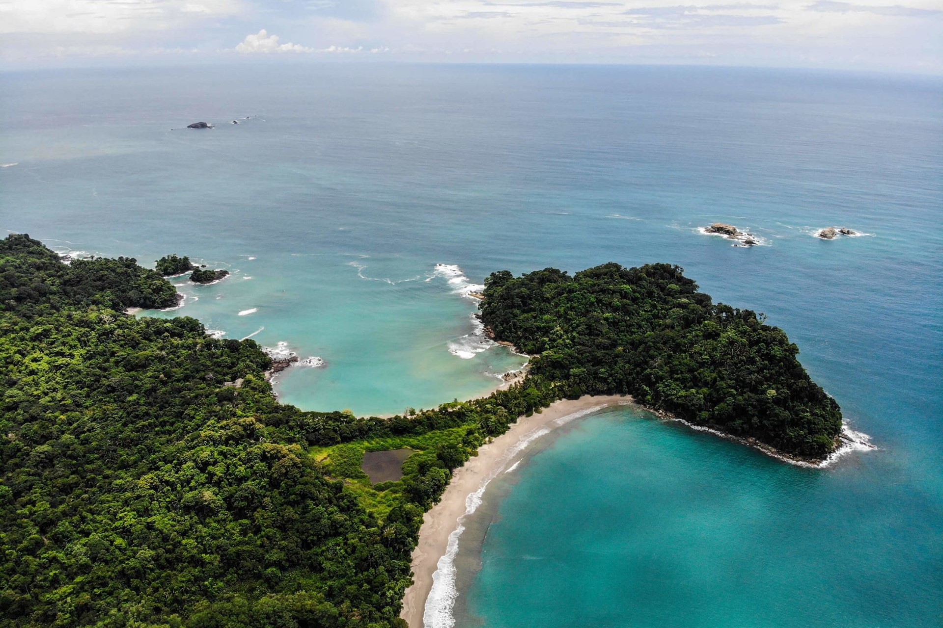 Aerial view of a lush tropical Costa Rican coastline with emerald waters caressing golden sandy beaches, embraced by the dense greenery of a forest.