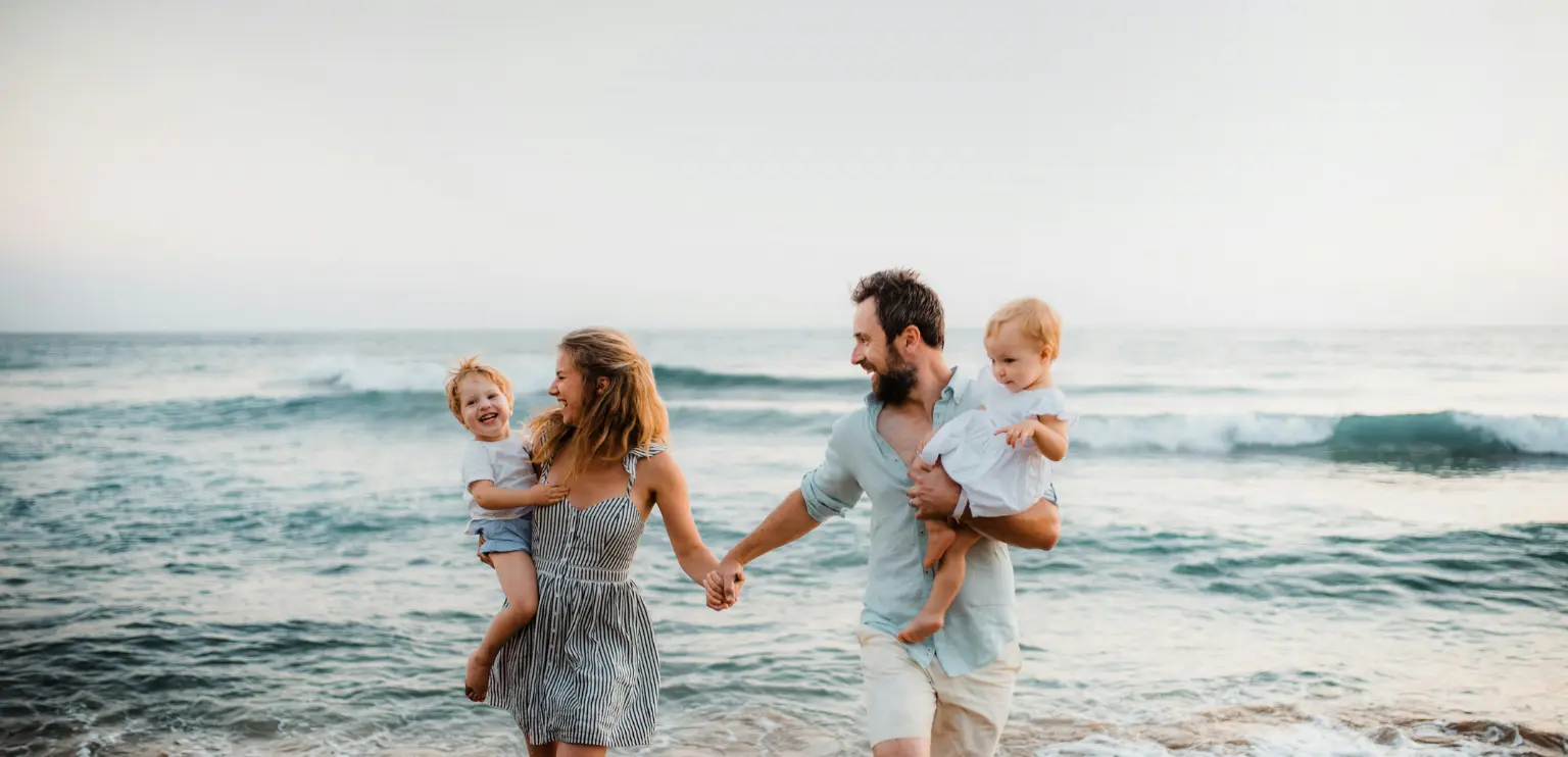 Family with two young children walking barefoot on the beach at sunset in Costa Rica