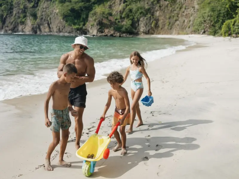 Family walking along a tropical beach in Costa Rica with kids carrying beach toys