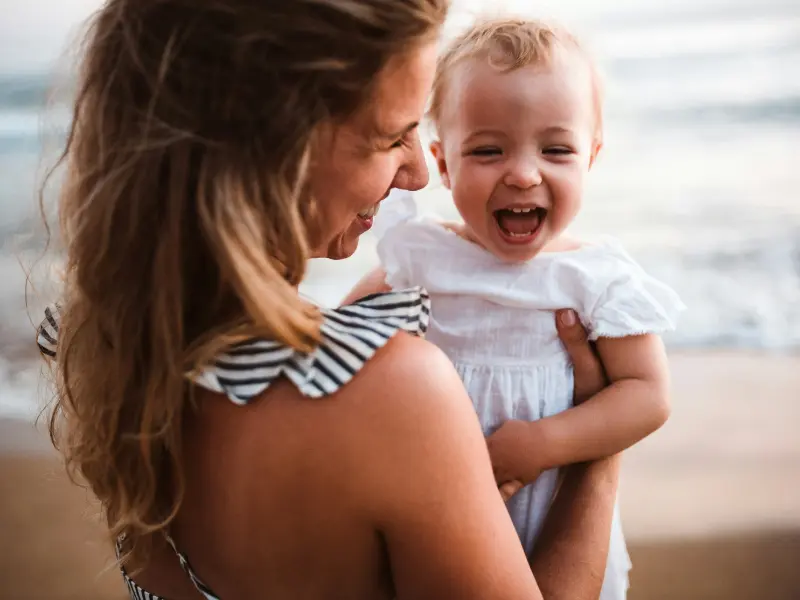 Smiling mother holding her laughing baby at sunset on a Costa Rica beach