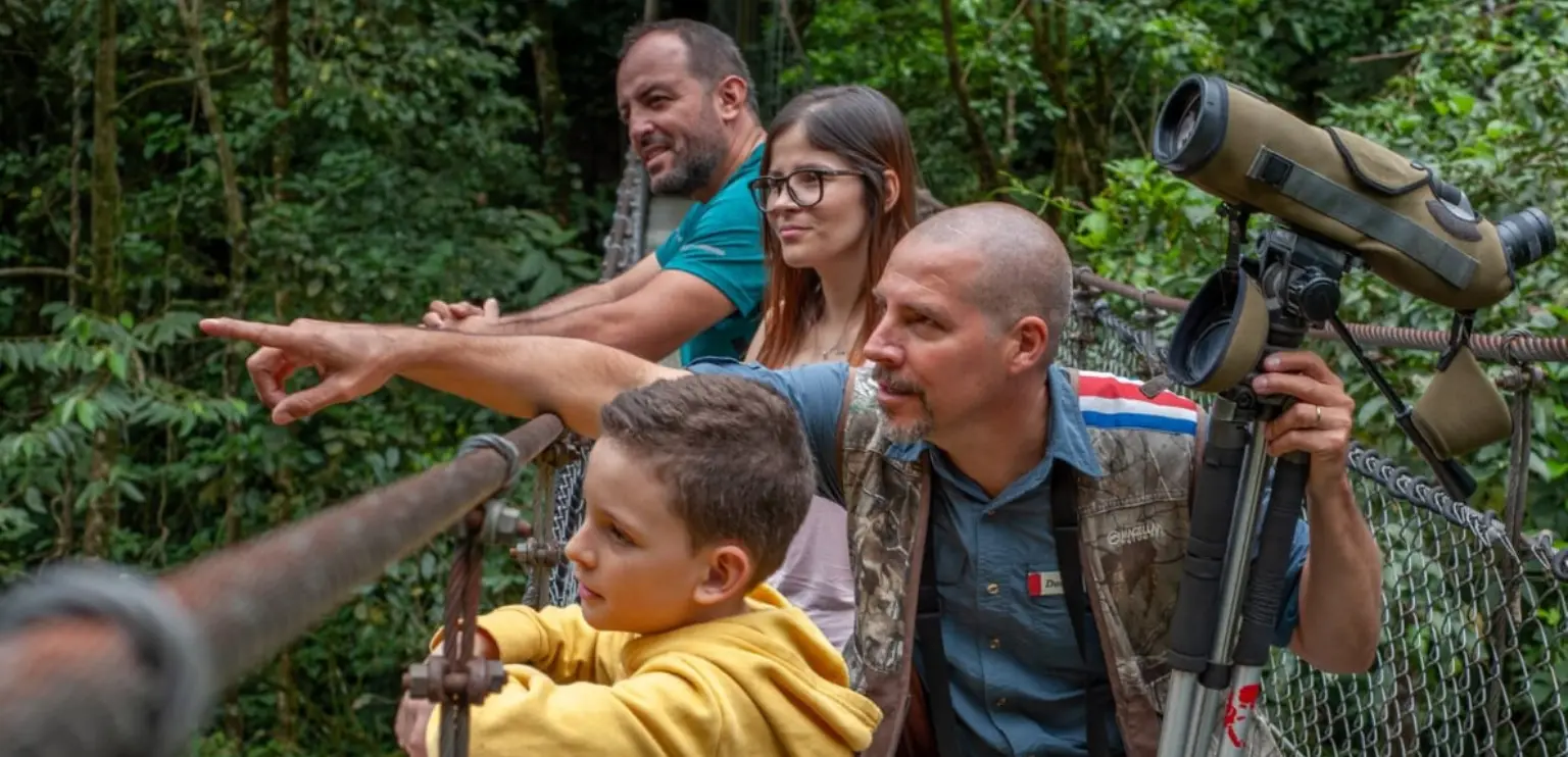 Family and naturalist guide observing wildlife on a hanging bridge in the Costa Rican rainforest