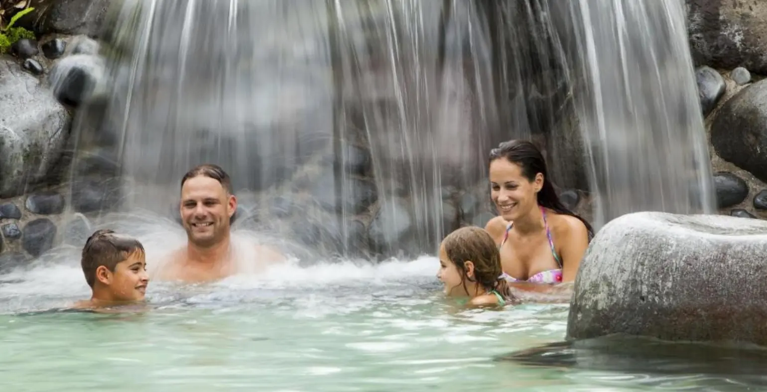 Family with kids enjoying hot springs under a waterfall in Costa Rica