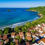 Aerial view of Las Catalinas beach town with red-roofed villas, tropical forest, and turquoise ocean in Guanacaste, Costa Rica.