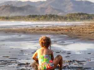 Little girl sitting on a quiet beach in Manuel Antonio Costa Rica, looking at the ocean during a peaceful family moment.
