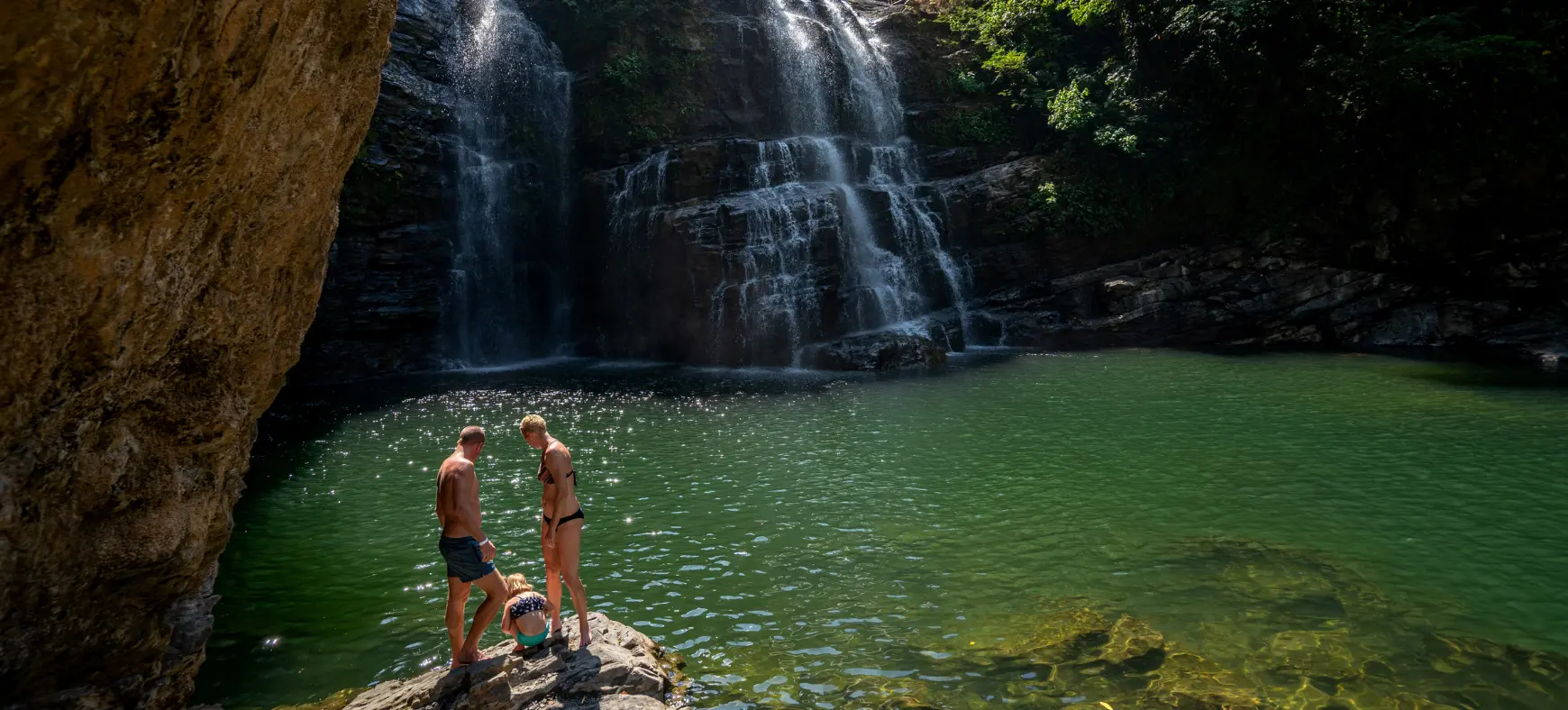 Family sitting on rocks by a jungle waterfall in Costa Rica